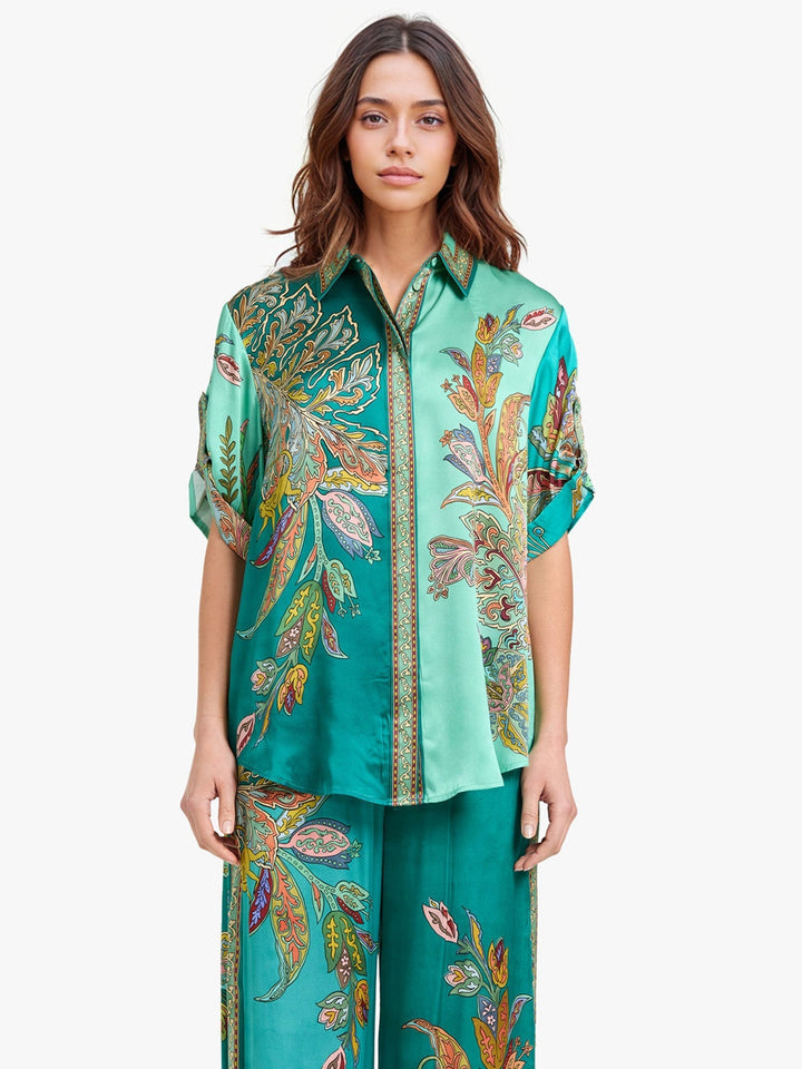 Model wearing a vibrant green two-piece set with intricate paisley patterns, posing in a studio with a white background.