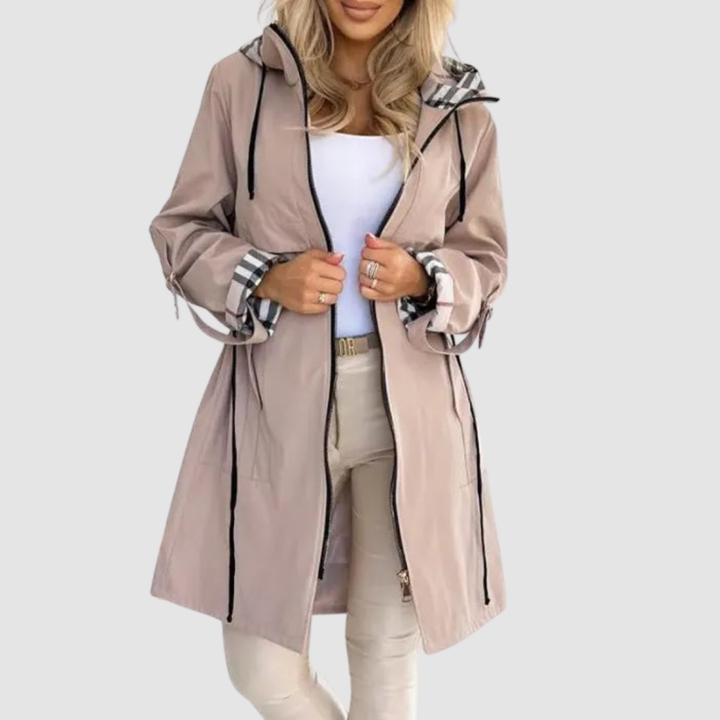 Tan waterproof zip coat with plaid-lined hood and cuffs, worn over a white top and beige leggings, against a white background.