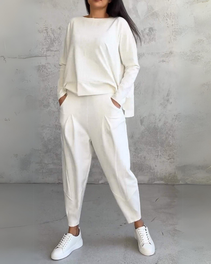 White lounge set with loose fit top and pants in a minimal gray studio setting.