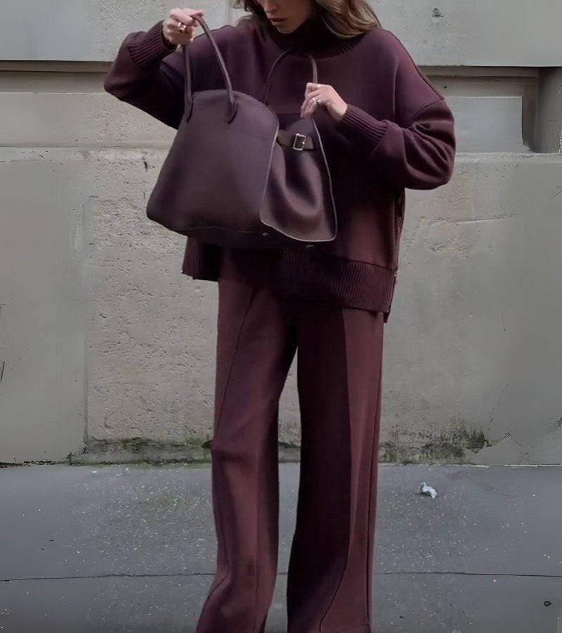 Close-up of a woman in a burgundy two-piece set, holding a large bag on a city street.