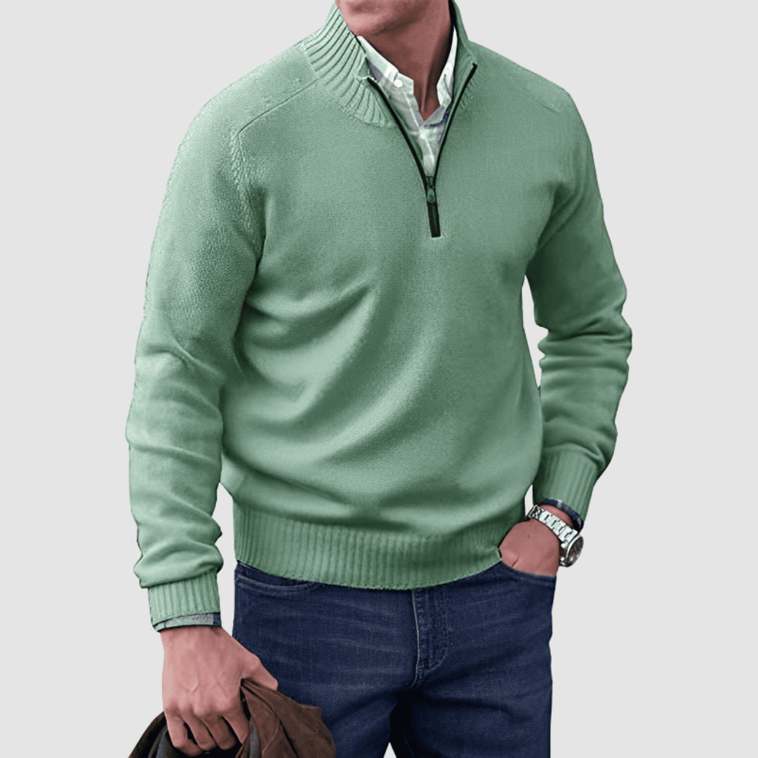 Model in green zip pullover with ribbed collar and cuffs, holding a jacket. Paired with jeans, set against a plain background.