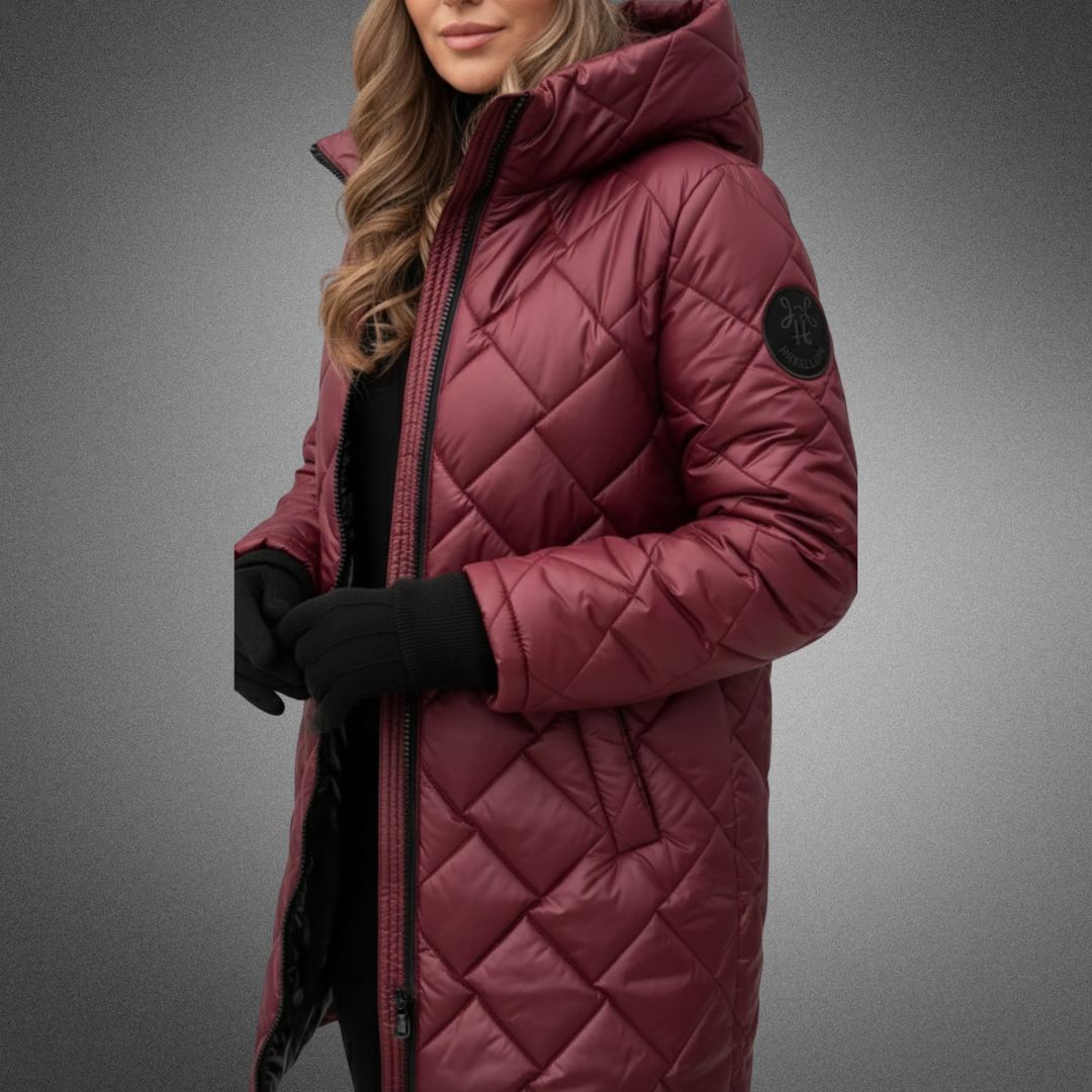 Woman in burgundy quilted jacket with hood in studio, wearing black gloves on a gradient background.
