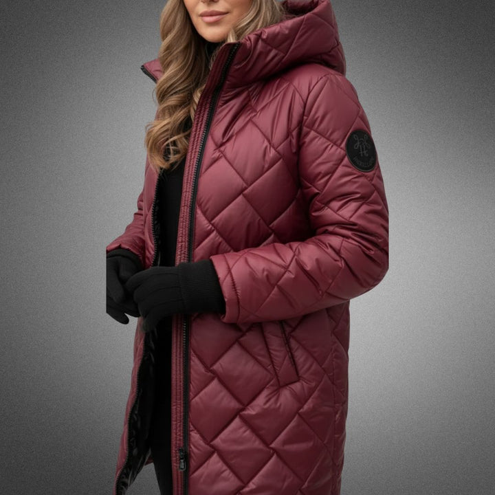 Woman in burgundy quilted jacket with hood in studio, wearing black gloves on a gradient background.