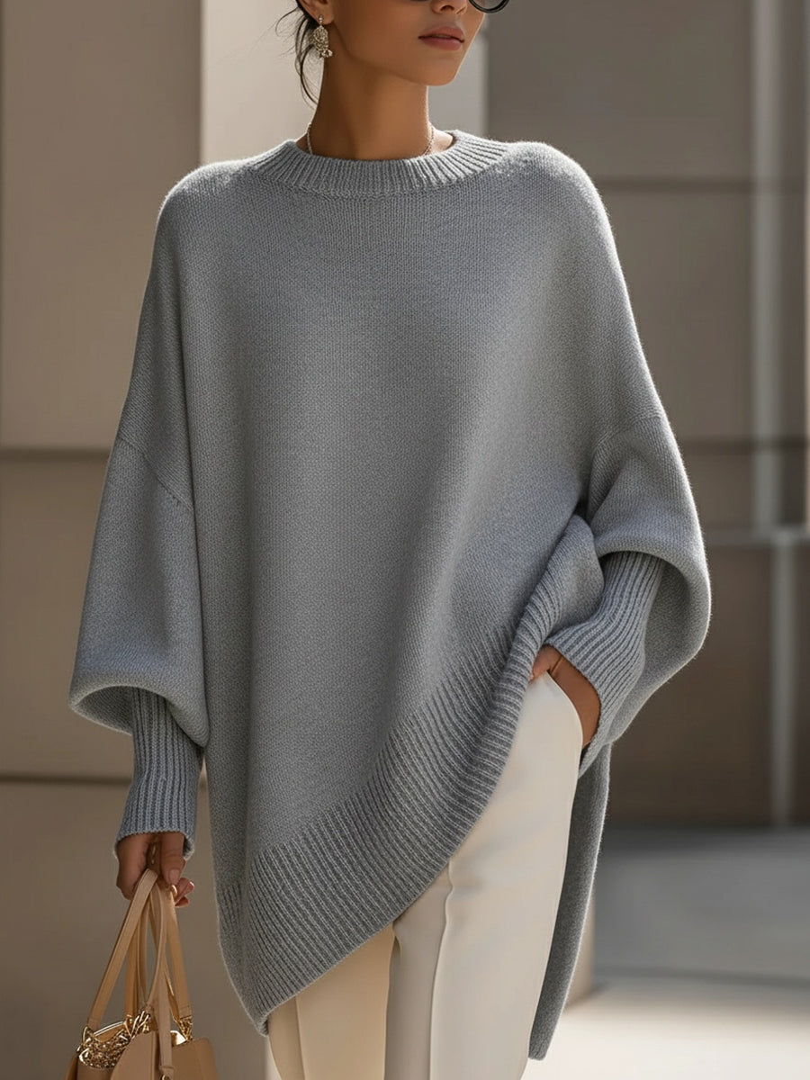 Woman in a loose gray sweater with ribbed hem and cuffs, paired with white pants, in an urban setting.