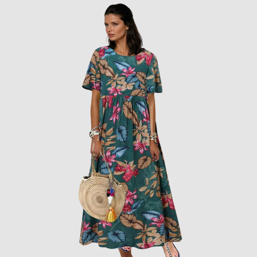 Woman in a teal summer dress with a bright floral design, accessorized with a round straw bag, in a studio environment.