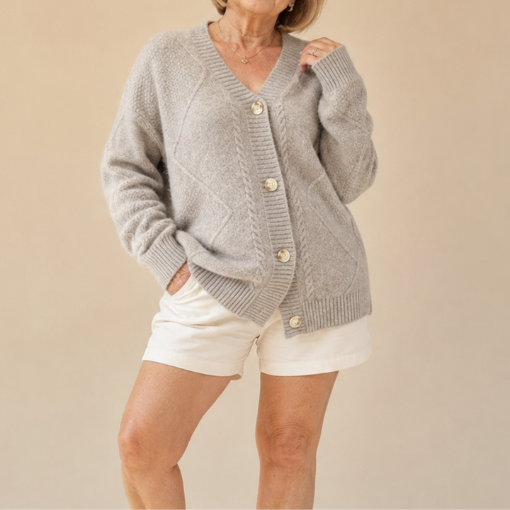 Model wearing a light gray knitted cardigan with buttons, combined with white shorts, in a neutral beige studio setting.