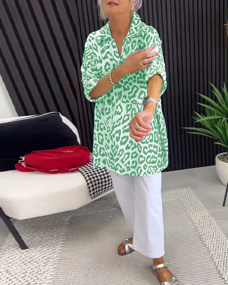 Green leopard print blouse with stylish collar, paired with white pants, in a modern indoor space with decorative elements.
