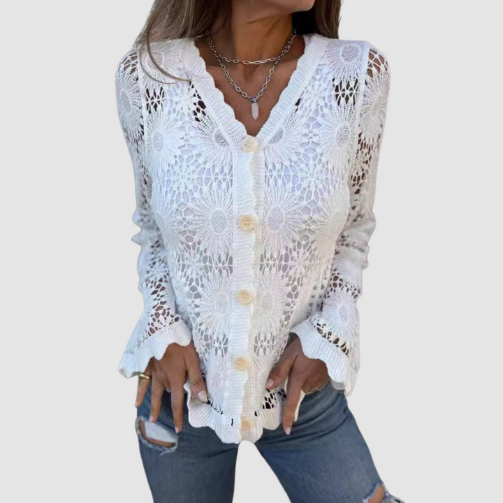 White lace V-neck cardigan with floral patterns, worn over blue jeans. Studio setting.