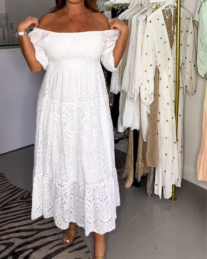 Woman adjusting off-shoulder white dress adorned with eyelets in a boutique environment.