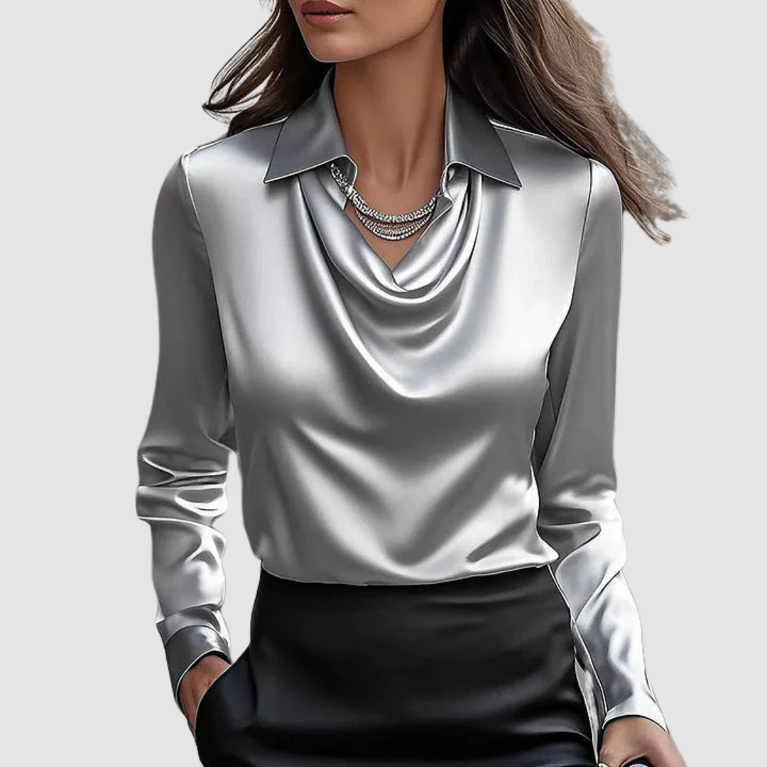 Elegant silver satin blouse with a draped neckline and long sleeves on a plain gray backdrop.