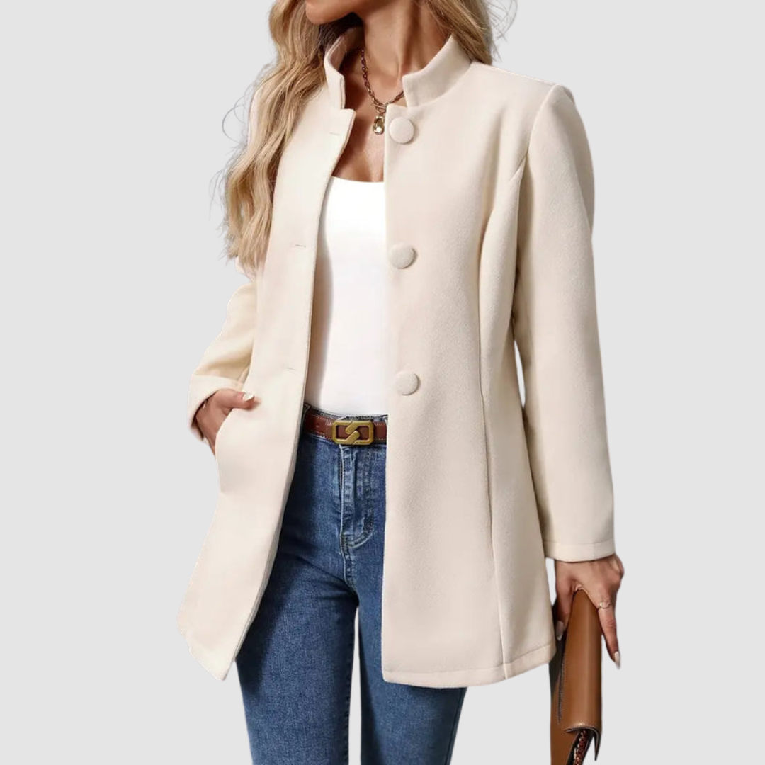 Light beige jacket with large buttons, white top underneath, jeans, holding clutch, plain background.