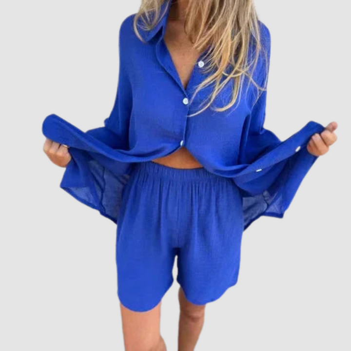 Model wearing a blue two-piece set with button-up shirt and shorts; neutral studio background.