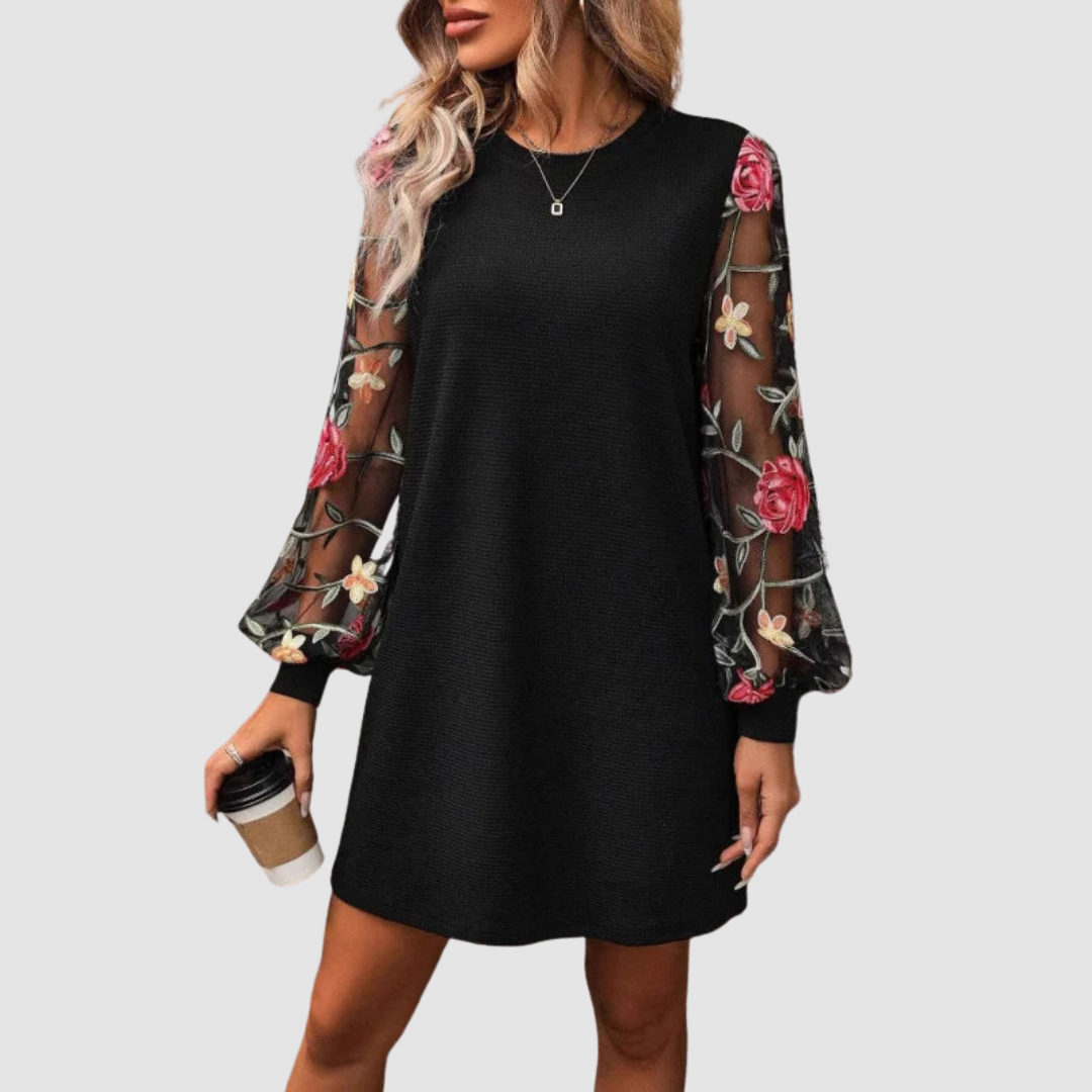 Woman in black dress with floral lace sleeves, holding a cup. Studio background.