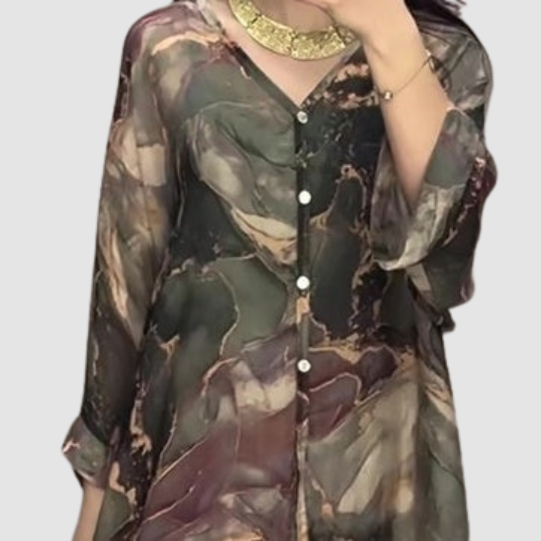 Close-up of model wearing an elegant printed top with button details, highlighted with jewelry, in a bright setting.