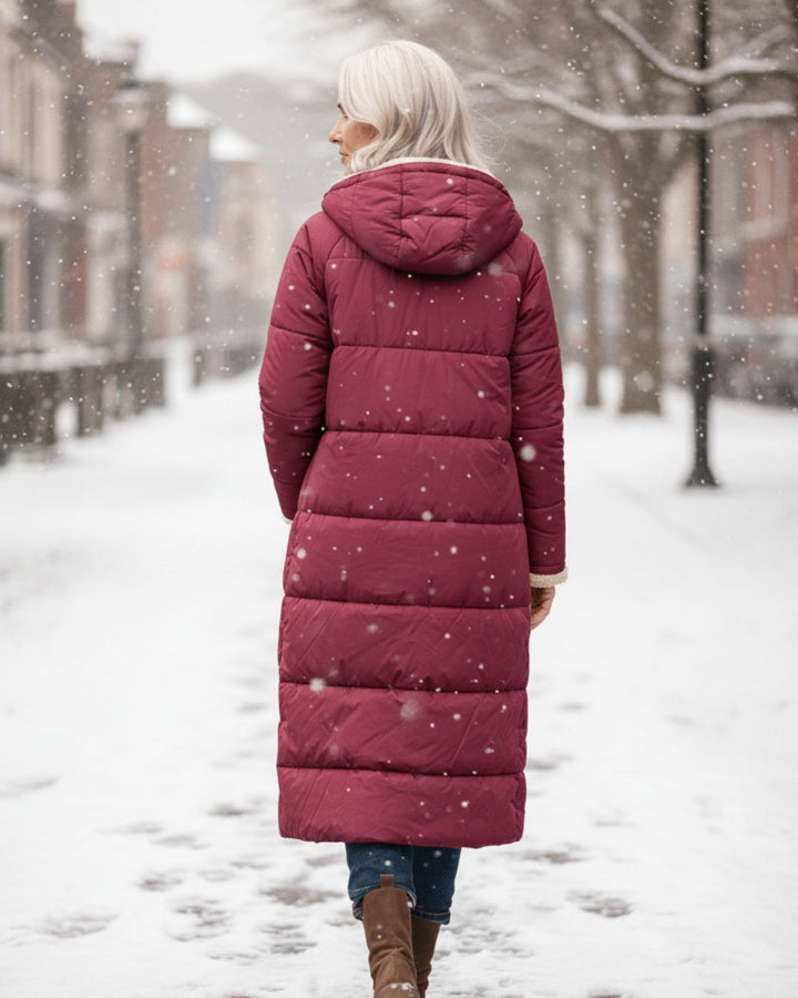 Back view of woman in red coat, walking through a snowy city street.