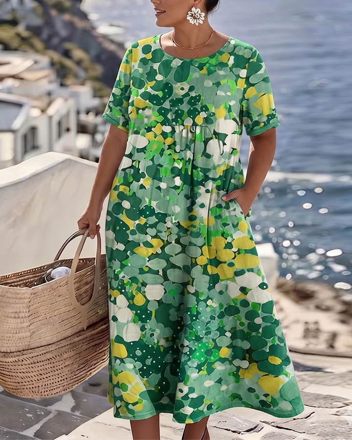 Woman wearing green floral dress near ocean, holding wicker bag, scenic seaside in background.