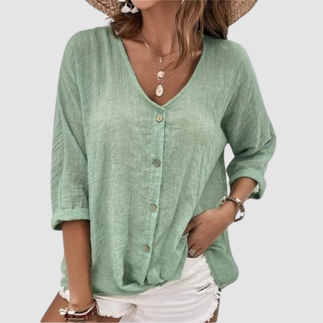 Woman wearing a green V-neck blouse with buttons, accessorized with necklaces and bracelets, paired with white shorts against a plain background.