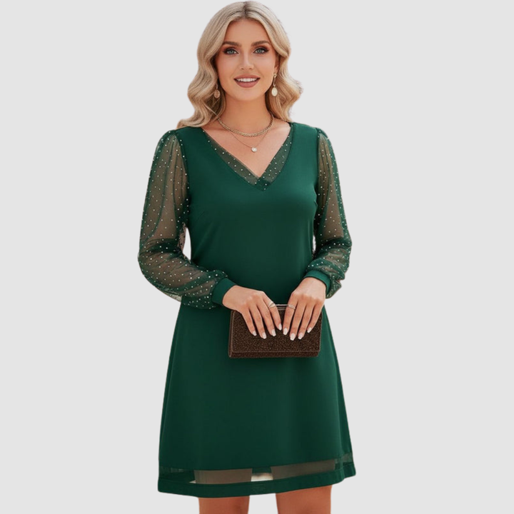 Elegant green dress with sheer polka dot sleeves, modeled holding a clutch in a studio setting.