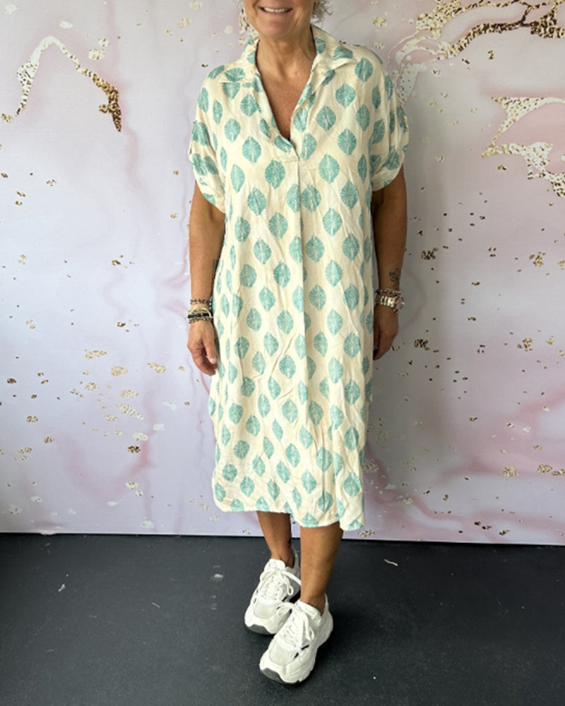 Person in light turquoise patterned dress, casual sneakers, in a studio setting with creatively styled walls.