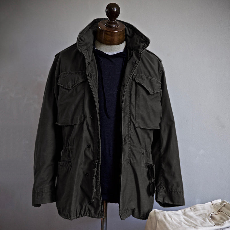 Dark field jacket on a mannequin with a hoodie underneath, set against a muted room background.