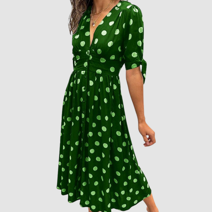 Green dress with white polka dots, V-neck, tied sleeves, knee-length, studio setting.