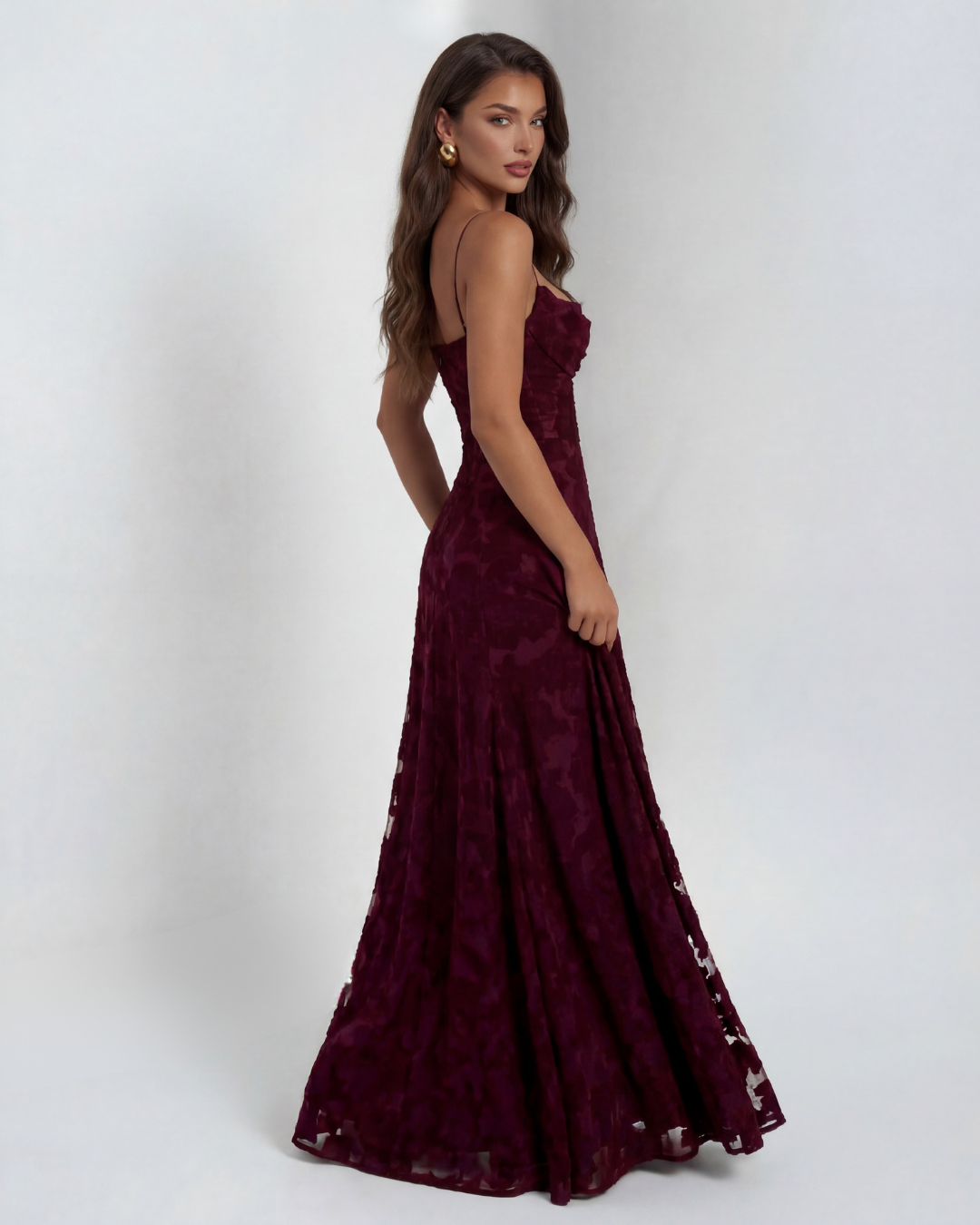 Side view of model in a burgundy floral maxi dress with thin straps, against a studio background.