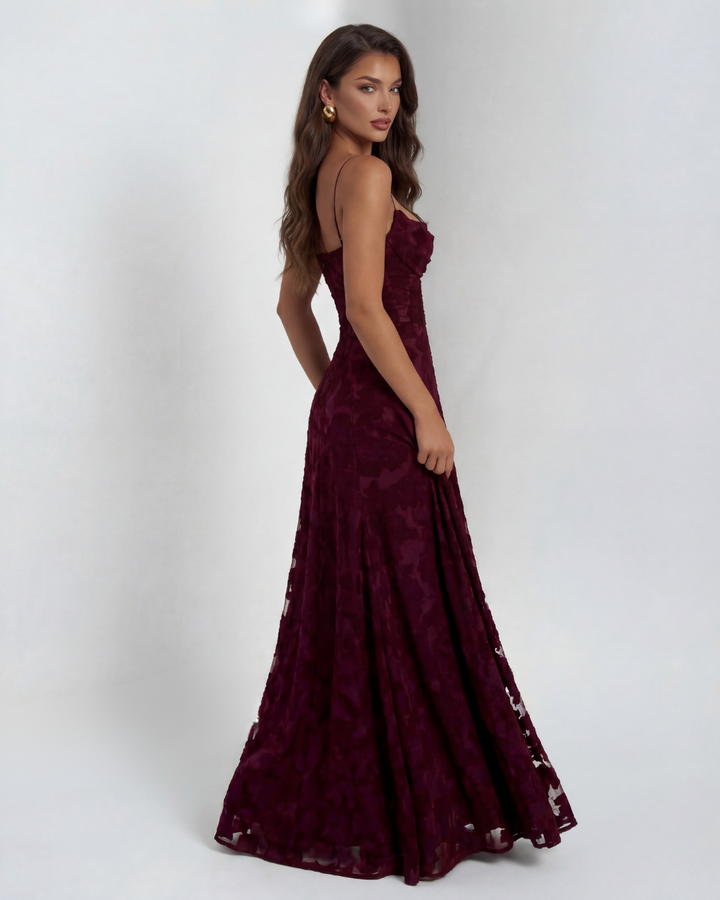 Side view of model in a burgundy floral maxi dress with thin straps, against a studio background.