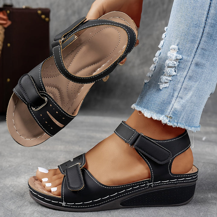 Black orthopedic sandal with sturdy straps and cushioned footbed, styled with ripped jeans on a gray floor.