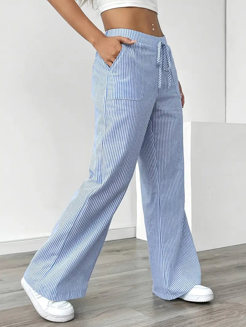 Side view of blue and white striped pants with pockets and drawstring, shown indoors with white sneakers.