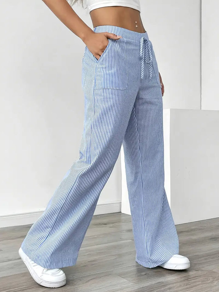 Side view of blue and white striped pants with pockets and drawstring, shown indoors with white sneakers.