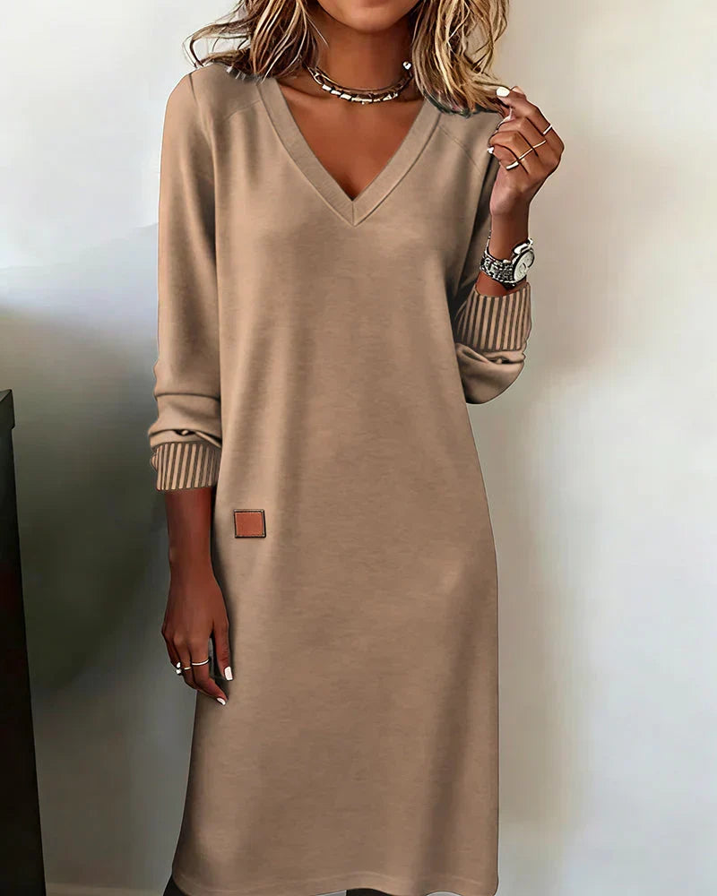 Beige cozy dress with V-neck and long sleeves, worn indoors.