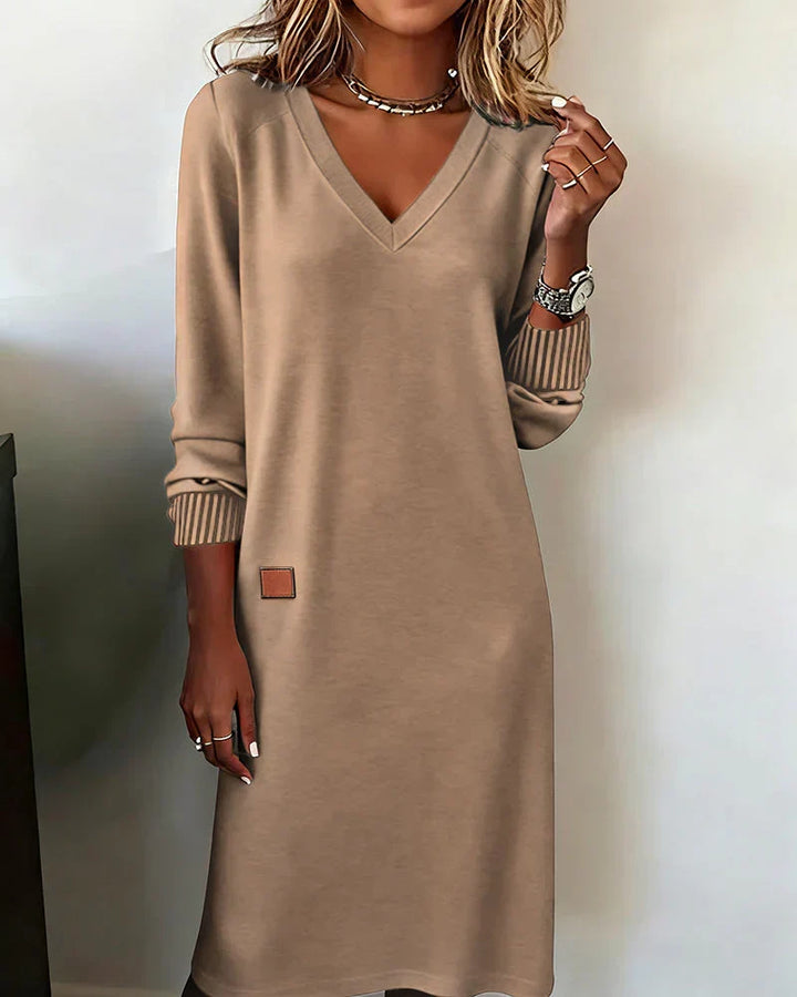 Beige cozy dress with V-neck and long sleeves, worn indoors.