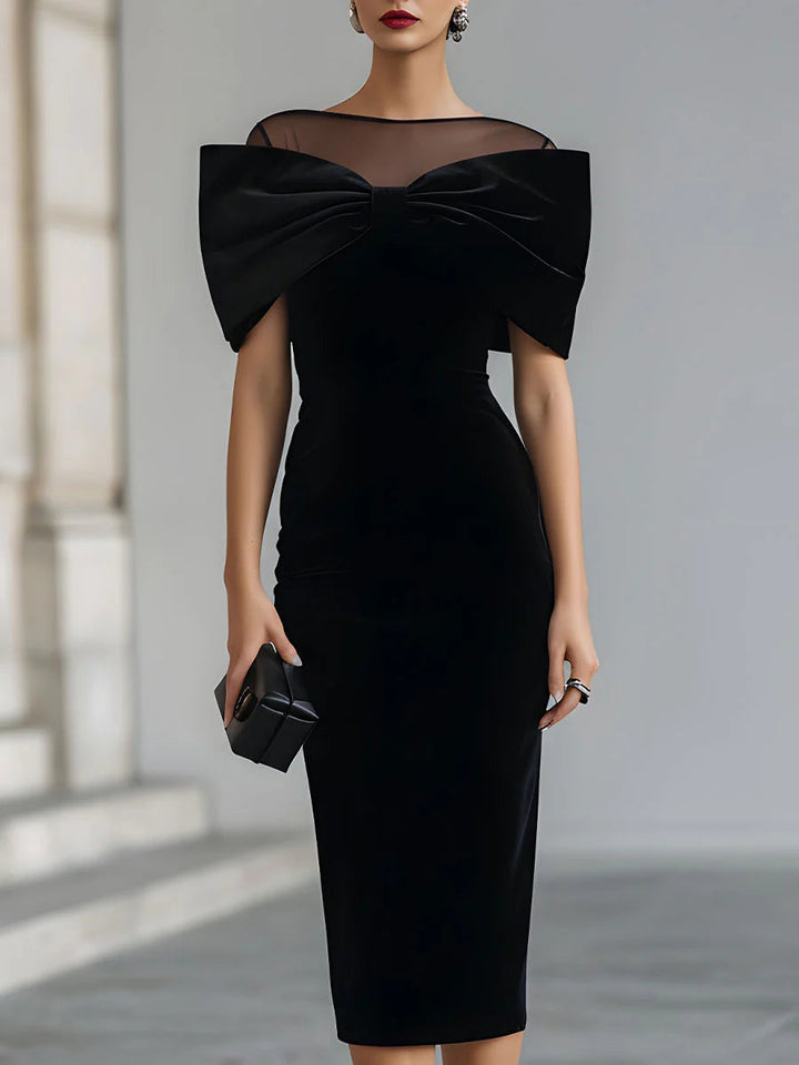 Elegant black midi dress with sheer neckline and large bow detail, held by a model against a neutral background.