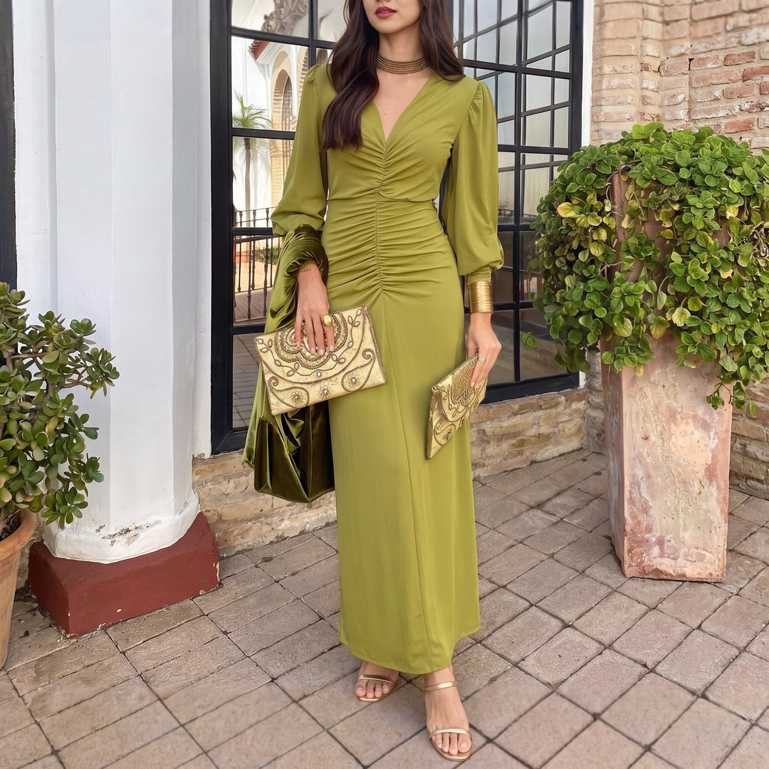 Chic olive green midi dress featuring ruched bodice and long sleeves, paired with gold jewelry, in a sunny patio setting.