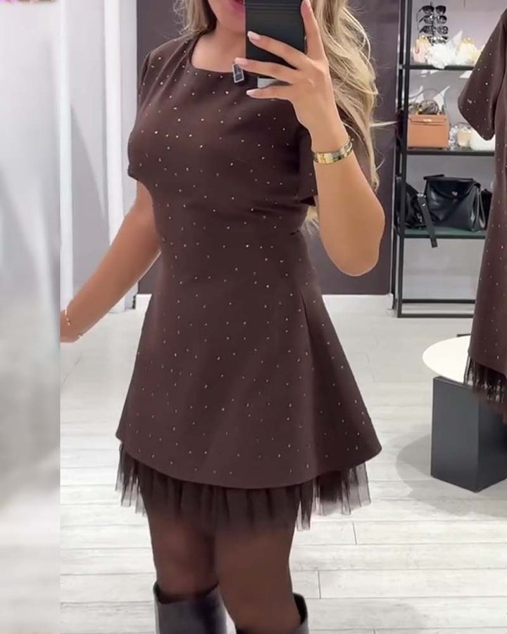 Model wearing a brown dress with sparkling details and layered tulle. Set in a boutique with light wood floors.