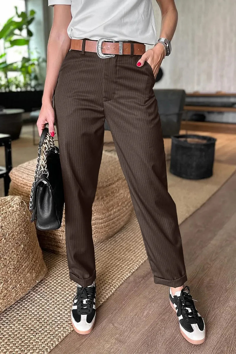 Brown pinstripe pants in a well-lit indoor room, paired with a brown belt and a handbag.
