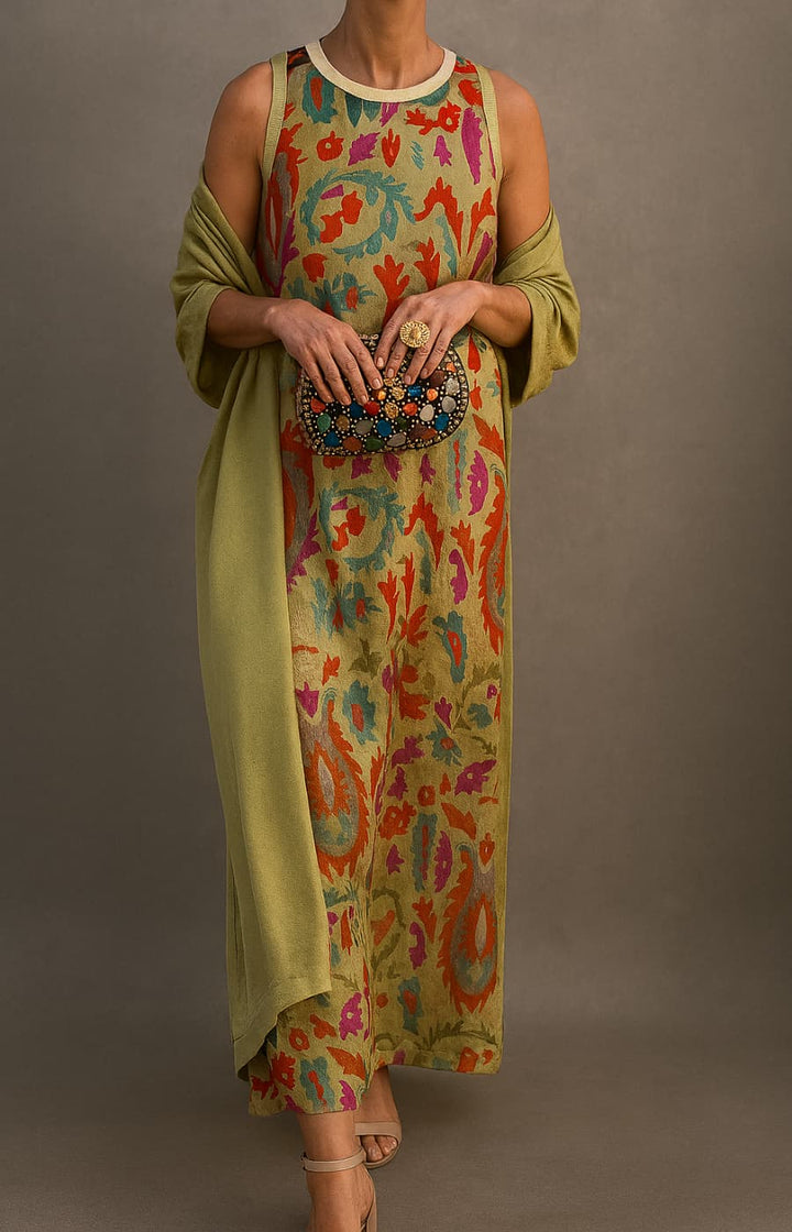 Model wearing colorful printed dress with green shawl, holding a decorative clutch in a studio setting.