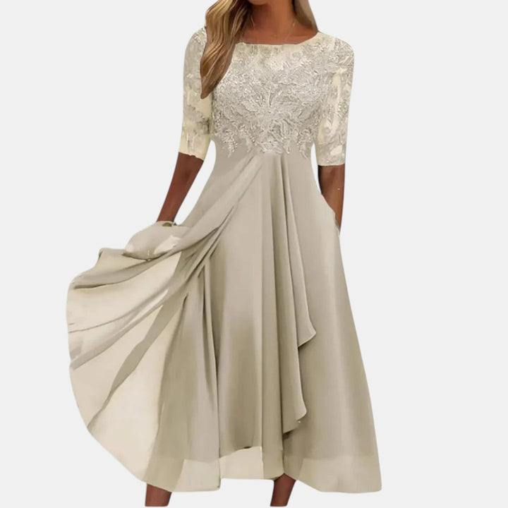Elegant beige dress with lace bodice and flowing skirt, studio background.