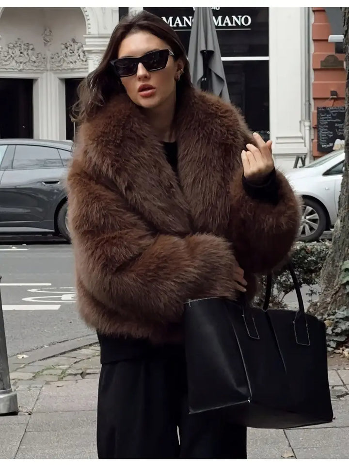 Person in a luxurious brown fur jacket holding a black handbag on a city street with classical architecture in the background.