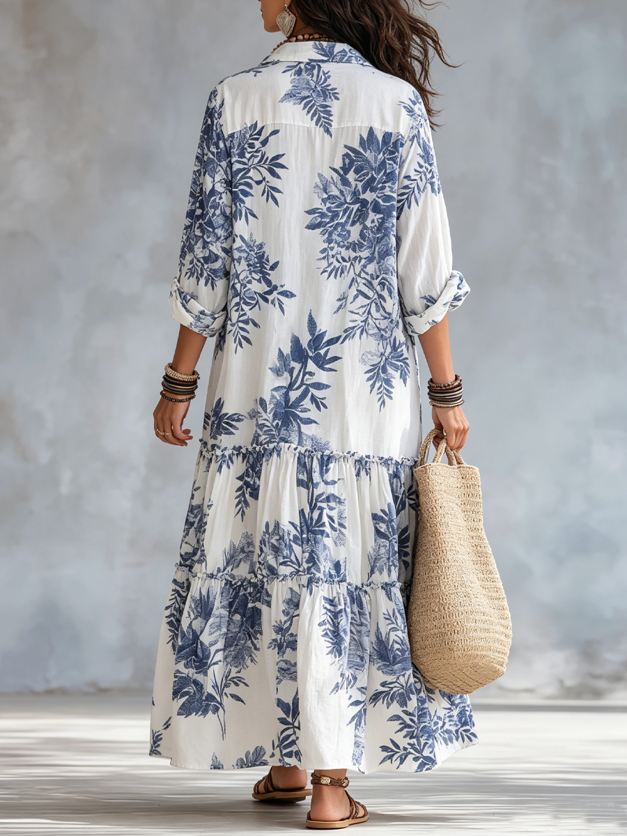 Back view of long white dress with blue floral patterns, paired with a woven bag, in a softly lit studio setting.