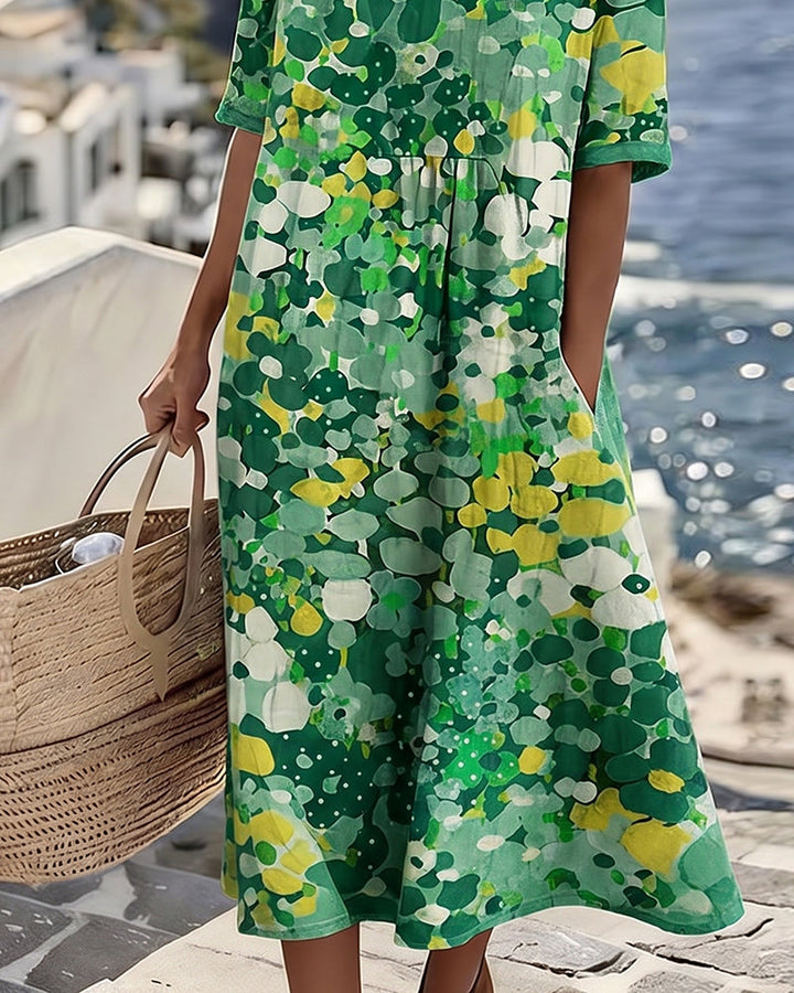 Close-up of green floral midi dress by the sea, model with wicker bag, coastal view in background.