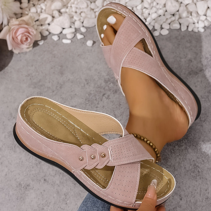 Pink orthopedic wedge sandals worn on feet, with a pink rose and white stones on a textured floor.