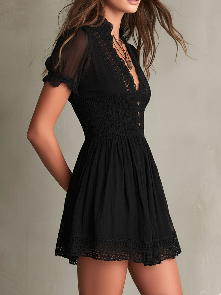 Side profile of black mini dress with lace-trim details, smocked waist, and flowy skirt in a studio setting.