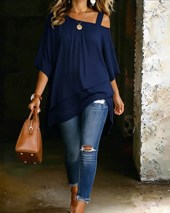 Navy blue asymmetrical blouse with off-shoulder straps paired with ripped jeans and brown handbag in rustic setting.
