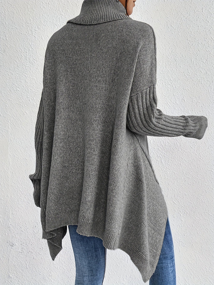 Back view of gray turtleneck sweater with ribbed sleeves, styled with jeans, against a plain white wall.