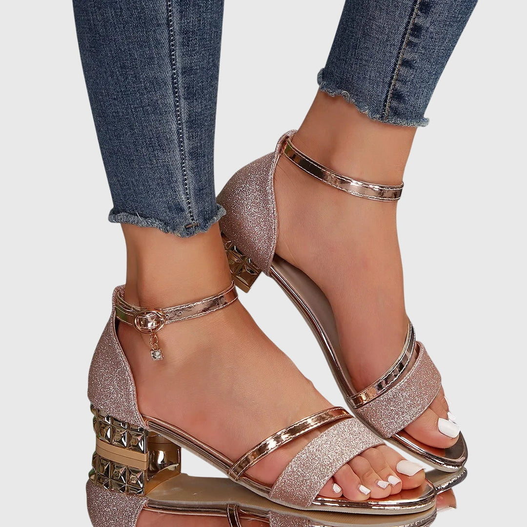 Pink glitter orthopedic heeled sandals with gold details, worn with frayed hem jeans, on a reflective surface.