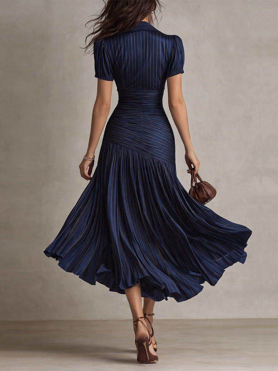 Back view of model in navy midi dress with detailed pleats and short sleeves, walking in a neutral studio.