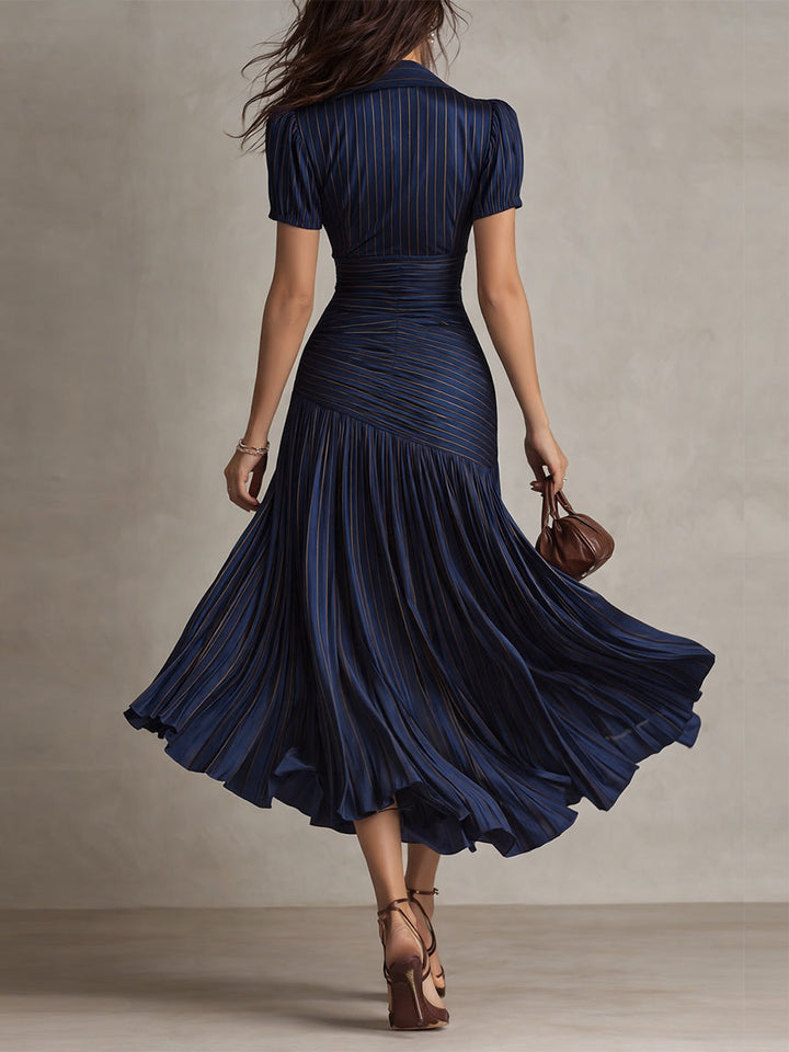 Back view of model in navy midi dress with detailed pleats and short sleeves, walking in a neutral studio.