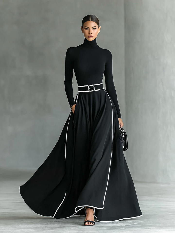 Elegant black long sleeve maxi dress with flowing skirt and white trim, accessorized with a black belt; studio setting.