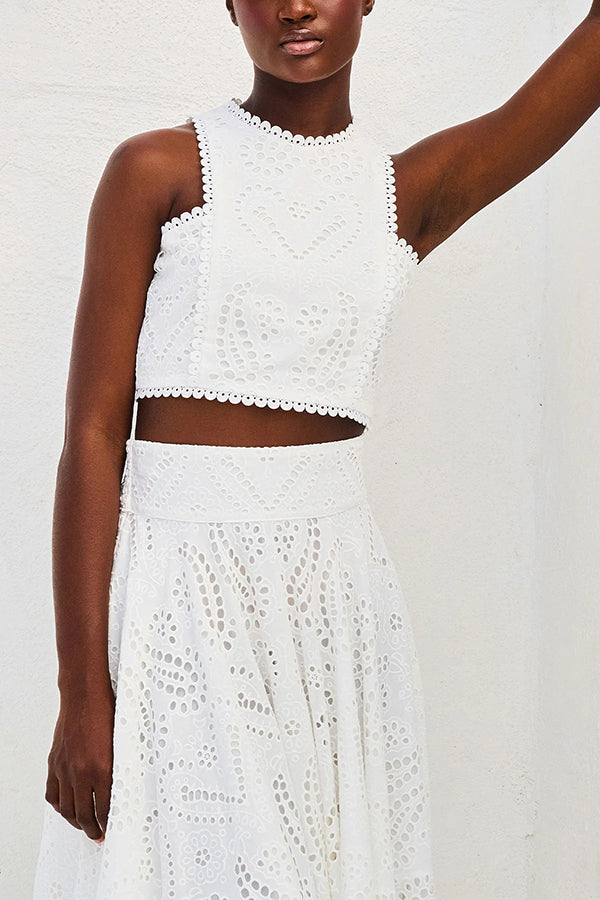 Close-up of a model in a white embroidered top and skirt set against a white wall.